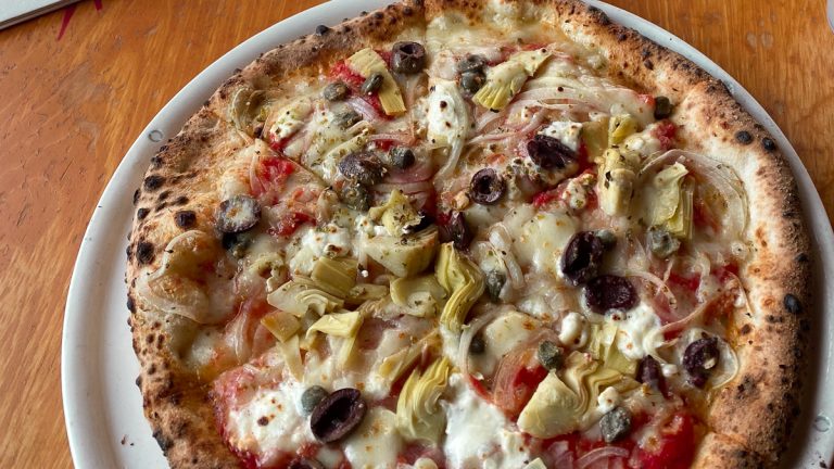 Wood-fired pizza topped with olives, artichokes, cheese, and tomato sauce at a restaurant in Eden Prairie.
